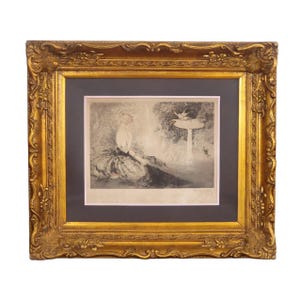 May include: An antique framed print featuring a woman seated near a fountain. The artwork is in grayscale, with a dark gray mat and a decorative gold-colored frame. The frame has ornate detailing.