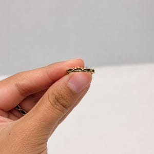 May include: A gold-toned metal ring featuring a continuous, repeating infinity or woven knot pattern around the entire band. The ring has a slim profile with a polished finish, showcasing an intricate, interconnected design that circles the finger.