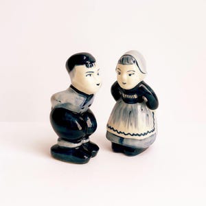 Peut inclure: Paire de figurines en céramique vintage représentant un homme et une femme en tenue hollandaise traditionnelle. L'homme est accroupi et la femme est debout. Les deux figurines sont peintes dans des tons de bleu, noir et blanc.