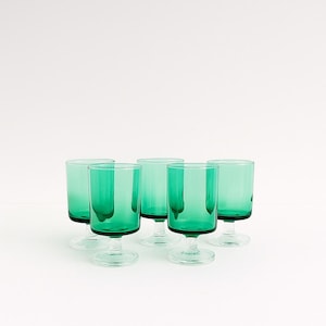 Peut inclure: Cinq verres à pied vert émeraude avec un bol cylindrique et un pied court. Les verres sont disposés sur une surface blanche, mettant en valeur leur couleur vibrante et leur design simple. La verrerie est idéale pour servir des boissons.