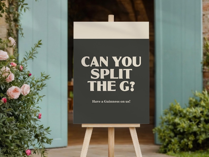 May include: A sign on a wooden easel with the text "CAN YOU SPLIT THE G?" in white, set against a dark grey background. The text "Have a Guinness on us!" is below. The sign is placed in front of a doorway and greenery.