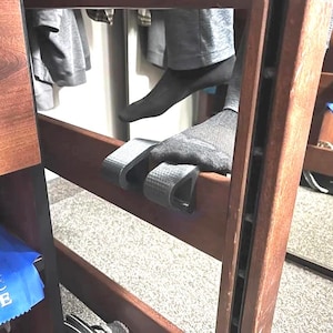 May include: A wooden bunk bed ladder with dark brown stain. The ladder has gray steps and a blue ribbon is visible on the side. A person's feet are on the ladder.