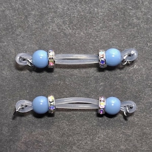 May include: Two pairs of eyeglass retainers. Each retainer features a light blue bead, a clear plastic cord, and a silver-colored ring with colorful rhinestones. The retainers are designed to secure eyeglasses.