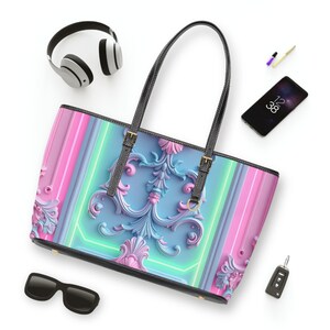 May include: A pastel-colored tote bag with a decorative floral design in shades of blue, pink, and green. The bag has black handles and trim, with gold-colored hardware. Other items include sunglasses, headphones, and a smartphone.