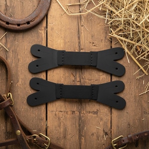 May include: Two black elastic connectors with bifurcated ends, each featuring two small circular holes on both sides. These flat, horizontal straps are designed with a central ribbed fabric section and smooth, shaped ends for attachment purposes.