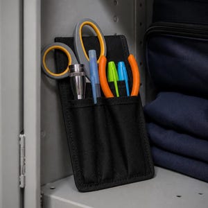 Puede incluir: Un organizador de herramientas de tela negra con múltiples ranuras verticales. La funda contiene unas tijeras con mangos grises y amarillos, una linterna de metal plateado, un bolígrafo de plástico transparente, un marcador verde, un marcador azul y unos alicates naranjas.