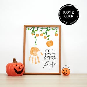 May include: A framed print featuring a handprint in orange paint, green vines, and small orange pumpkins. The text reads GOD PICKED ME FROM The patch. A large orange jack-o'-lantern and a small orange jack-o'-lantern sit in front of the frame.