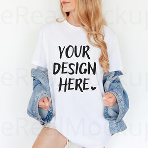 May include: White t-shirt with the text "YOUR DESIGN HERE" in a bold, black font. The model is wearing a light blue denim jacket. The overall aesthetic is casual and modern, perfect for showcasing custom designs.