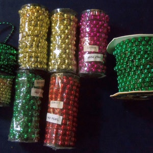 May include: Assortment of spools of metallic half pearl beads in green, gold, red, and pink. The spools are wrapped in clear plastic and labeled "Half Pearl".