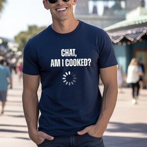 Könnte beinhalten: Ein marineblaues Kurzarm-T-Shirt mit dem weißen Text "CHAT, AM I COOKED?" auf der Brust. Unter dem Text befindet sich ein kreisförmiges Ladesymbol, das aus zwölf kleinen weißen Segmenten in einem Ringmuster besteht.