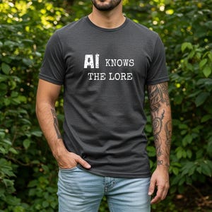 Könnte beinhalten: Ein dunkelgraues Kurzarm-T-Shirt mit dem weißen Schriftzug AI KNOWS THE LORE auf der Brust. Das Shirt hat einen Rundhalsausschnitt und eine normale Passform, kombiniert mit einer hellblauen Jeanshose.