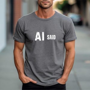 Peut inclure: Un t-shirt gris anthracite à manches courtes et col rond, arborant le texte blanc "AI SAID" imprimé au centre de la poitrine avec un effet vieilli. Le vêtement est composé d'un tissu chiné avec une coupe standard et un col rond simple.