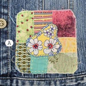 May include: A colorful, patchwork fabric applique with a floral design. The applique features a yellow pear shape with white flowers and red centers, stitched onto a background of various patterned fabrics in green, pink, and blue. The applique is sewn onto a denim jacket.