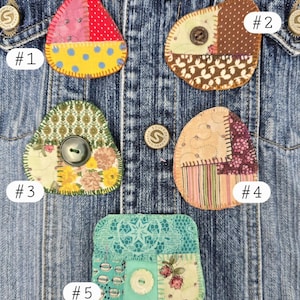 May include: Close-up of a denim jacket adorned with five unique, handmade fabric patches. Each patch features a patchwork design with various patterns, colors, and textures, including polka dots, floral prints, and stripes. The patches are numbered and secured with buttons.