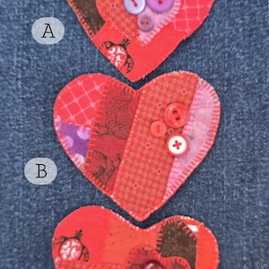 May include: Three handmade heart-shaped fabric patches with decorative stitching. Each heart is red with patchwork patterns and embellished with buttons. The patches are arranged on a blue denim background.