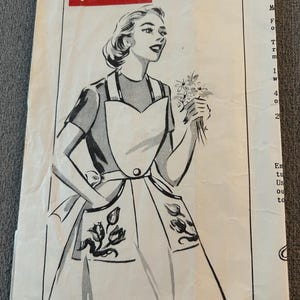May include: Vintage sewing pattern titled "parade pattern" featuring a black and white illustration of a woman wearing an apron and holding flowers. The apron has floral designs on the pockets. The pattern is on aged paper.