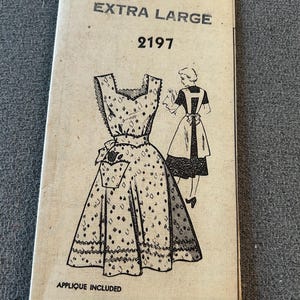May include: A vintage sewing pattern envelope labeled EXTRA LARGE 2197. The front features a black and white line drawing of a sleeveless dress with a diamond pattern, a pocket, and a bow at the waist. The text APPLIQUE INCLUDED is printed at the bottom.