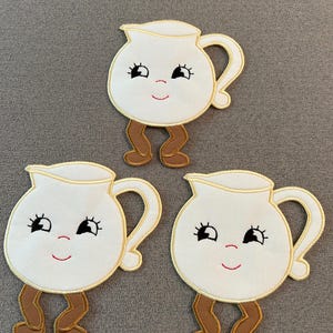 May include: Three white coffee pot appliqués with smiling faces, black eyelashes, and brown legs. Each pot has a gold outline and a red smiling mouth. The appliqués are on a gray background.