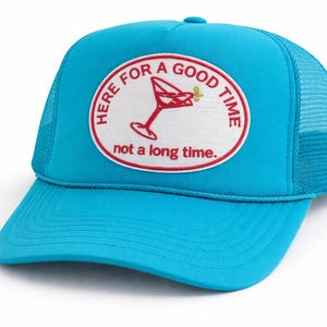May include: A turquoise trucker hat with a white and red circular patch. The patch features a red cocktail glass and the text "HERE FOR A GOOD TIME" and "not a long time."