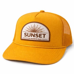 May include: Mustard yellow trucker hat with a mesh back and a curved brim. The front features a patch with the word "SUNSET" in a bold font, with a sunburst design above it. A stylish accessory.