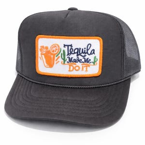 May include: Charcoal gray trucker hat with a rectangular patch featuring a cocktail, cactus, and the text "Tequila Made Me Do It" in white and orange. The hat has a curved brim and mesh back.