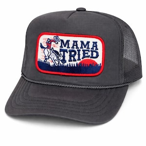 Op de afbeelding: Antracietgrijze truckerpet met een patch met een rodeo-scène en de woorden "MAMA TRIED" in rood, wit en blauw. De pet heeft een mesh achterkant en een gebogen klep.