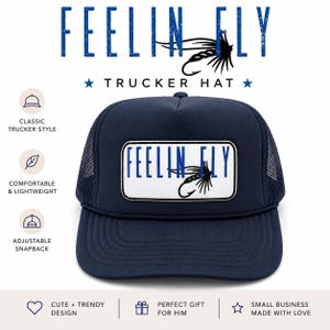 Può includere: Cappellino da camionista blu navy con retro in rete e toppa rettangolare bianca. La toppa presenta le parole "FEELIN FLY" in blu, con una grafica di mosca da pesca in bianco e nero. Il cappello ha anche il testo "TRUCKER HAT".