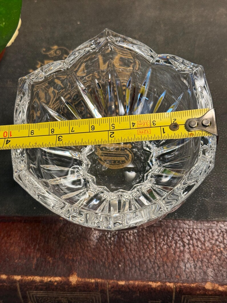 May include: A clear, faceted crystal ashtray with a starburst design. The ashtray is approximately 4 inches wide. The edges are cut with a decorative pattern. The ashtray is sitting on a dark surface.