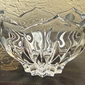 May include: A clear, decorative glass bowl with a unique, textured design. The bowl has a star-shaped base and a scalloped rim. The glass reflects light, creating a sparkling effect. The bowl is likely used for decorative purposes.