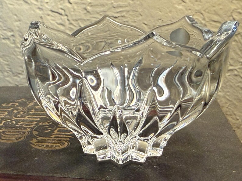 May include: A clear, decorative glass bowl with a unique, textured design. The bowl has a star-shaped base and a scalloped rim. The glass reflects light, creating a sparkling effect. The bowl is likely used for decorative purposes.