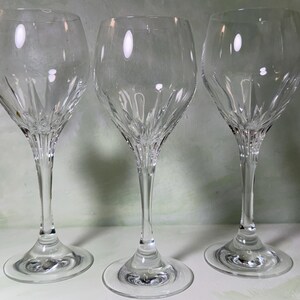 May include: Three clear glass wine glasses with a rounded bowl and a slender stem. Each glass features a decorative cut pattern at the base of the bowl, consisting of vertical lines that radiate upward, creating a textured, light-reflecting effect.
