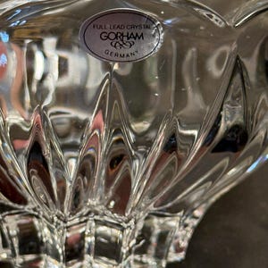 May include: Close-up of a clear, lead crystal bowl with a scalloped edge. The bowl has a textured, geometric design and a sticker that reads "FULL LEAD CRYSTAL GORHAM GERMANY."