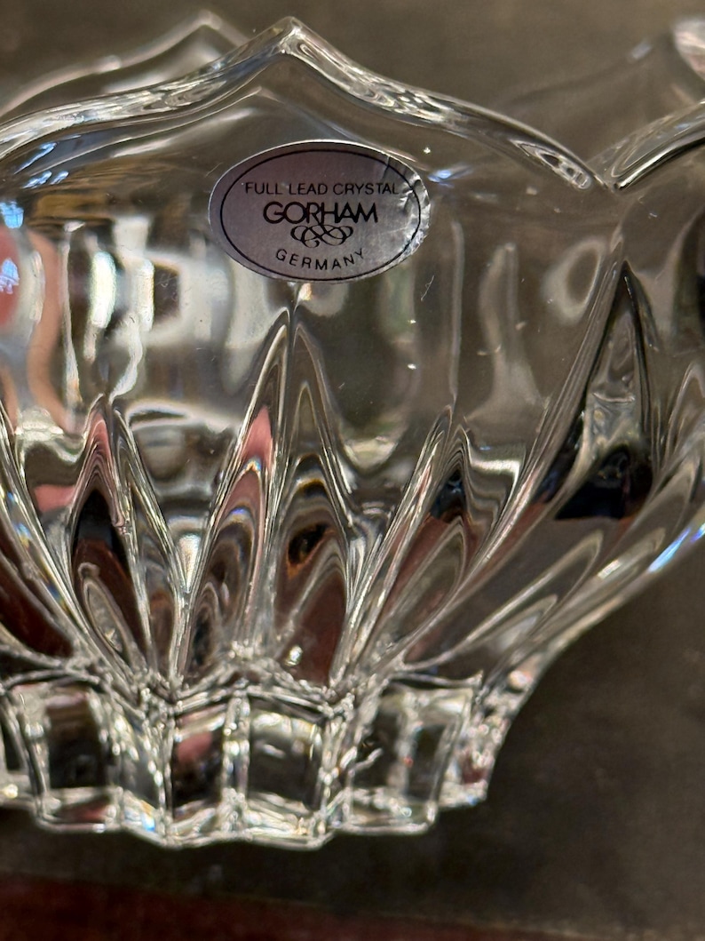 May include: Close-up of a clear, lead crystal bowl with a scalloped edge. The bowl has a textured, geometric design and a sticker that reads "FULL LEAD CRYSTAL GORHAM GERMANY."