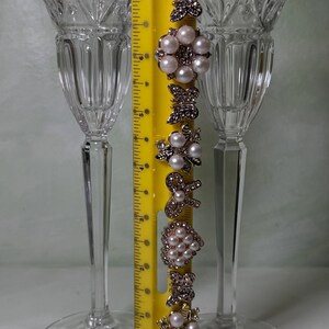 May include: Two clear crystal stemmed glasses with vertical fluting and a yellow ruler measuring approximately 7 inches in height. A vertical row of decorative metal embellishments featuring faux pearls and rhinestones in butterfly and floral shapes.