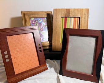 May include: Four rectangular picture frames of varying designs. One is dark wood with three square cutouts, one has a light wood grain, one features a light brown finish with a purple circle pattern, and one has a red and black curved frame.