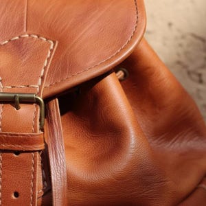 Close up of handmade brown leather backpack with textured full grain leather, vintage buckle closure and detailed stitching, rustic artisan leather bag craftsmanship