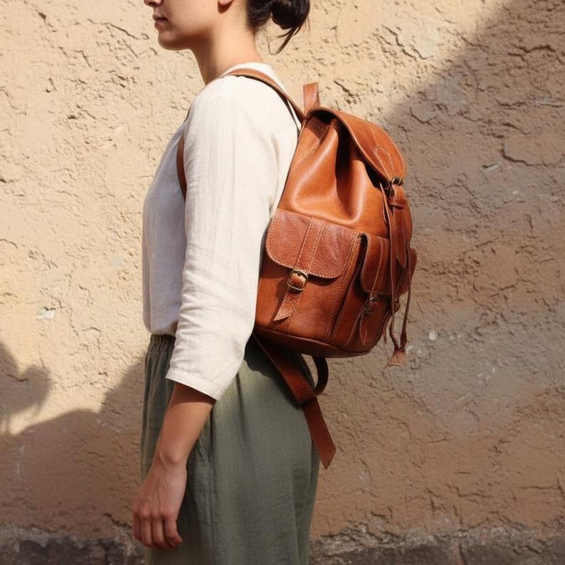 Woman wearing handmade brown leather backpack, vintage boho travel rucksack with adjustable straps and front pockets, stylish leather bag for everyday carry, work and college