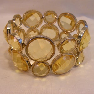 May include: A gold tone stretch bracelet with large, faceted, yellow glass stones.