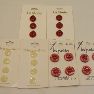 May include: Assortment of sewing buttons on cards. Includes red ladybug-shaped buttons, cream-colored round buttons, and red buttons with white polka dots. Some cards are labeled "La Mode", "Streamline", and "la petite".