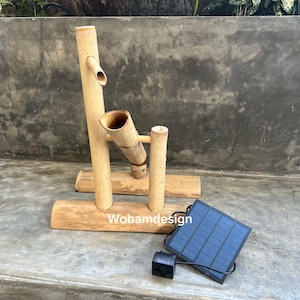 May include: A bamboo water fountain with a solar panel. The fountain is made of natural bamboo and features a vertical spout and a horizontal spout. The solar panel is black and blue. The base is made of bamboo.