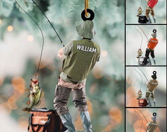 May include: A fishing-themed ornament featuring a fisherman with a fishing rod, a caught fish, and a tackle bag. The fisherman wears a green vest with the name "WILLIAM" on the back. The ornament is suspended by a gold string.