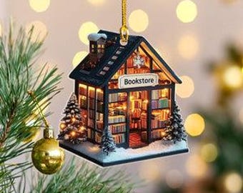 May include: A miniature bookstore Christmas ornament. The ornament is a small house with a black roof, a chimney, and a sign that reads "Bookstore." The interior is lit up, showing bookshelves filled with books. Two small Christmas trees flank the building.