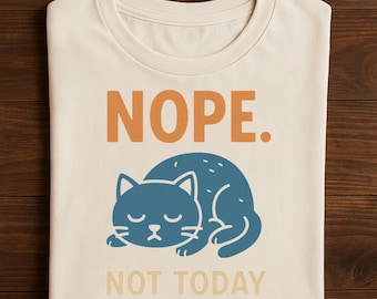 Puede incluir: Camiseta color crema con las palabras "NOPE. NOT TODAY" en letras naranjas y beige. Un gráfico de un gato azul está acurrucado debajo del texto, con los ojos cerrados, transmitiendo un estado de ánimo somnoliento.