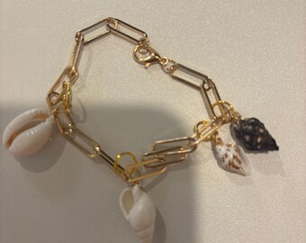 May include: Gold-toned chain bracelet featuring a series of paperclip-style links. The bracelet is adorned with several small seashells in shades of white, brown, and black, creating a coastal theme. The bracelet has a lobster clasp closure.
