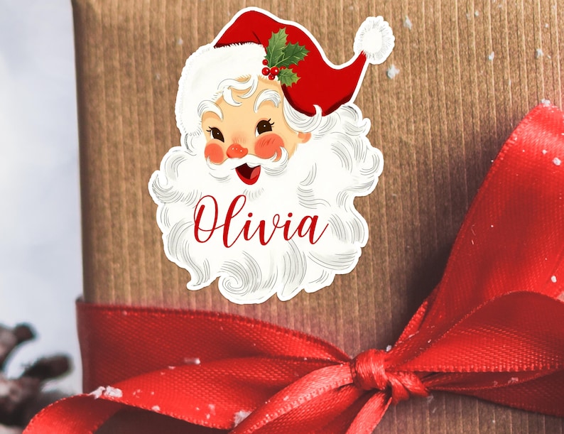 May include: A Santa Claus sticker with a red hat, white beard, and the name "Olivia" in red script. The sticker is placed on a wrapped gift with a red ribbon.