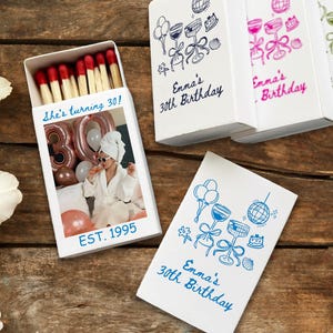 May include: White matchbox with red-tipped matches, featuring a photo of a person celebrating a birthday. Text on the box reads "She's turning 30!" and "EST. 1995." Additional boxes with "Emma's 30th Birthday" are visible.