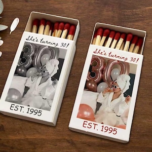 May include: Two white matchboxes with red-tipped matches. Each box features a black and white photo of a person celebrating a birthday, with the text "She's turning 30!" and "EST. 1995" in red.