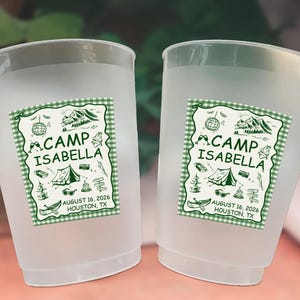 May include: Two frosted plastic cups with a green and white gingham label. The label reads "CAMP ISABELLA" with camping-themed illustrations and the date "AUGUST 16, 2026, HOUSTON, TX."