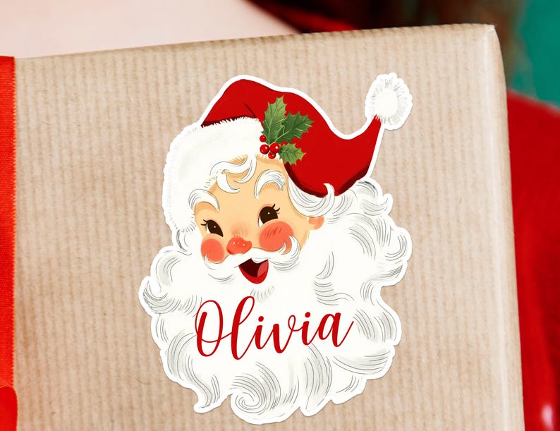 May include: A sticker featuring a vintage Santa Claus design with a red hat, white beard, and the name "Olivia" in red script. The sticker is placed on a wrapped gift with a red ribbon.