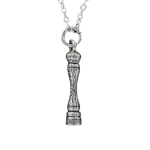 May include: A silver-colored pendant necklace featuring a miniature pepper grinder charm. The charm has a detailed design with the word "pepper" engraved on the side. The necklace chain is also silver.